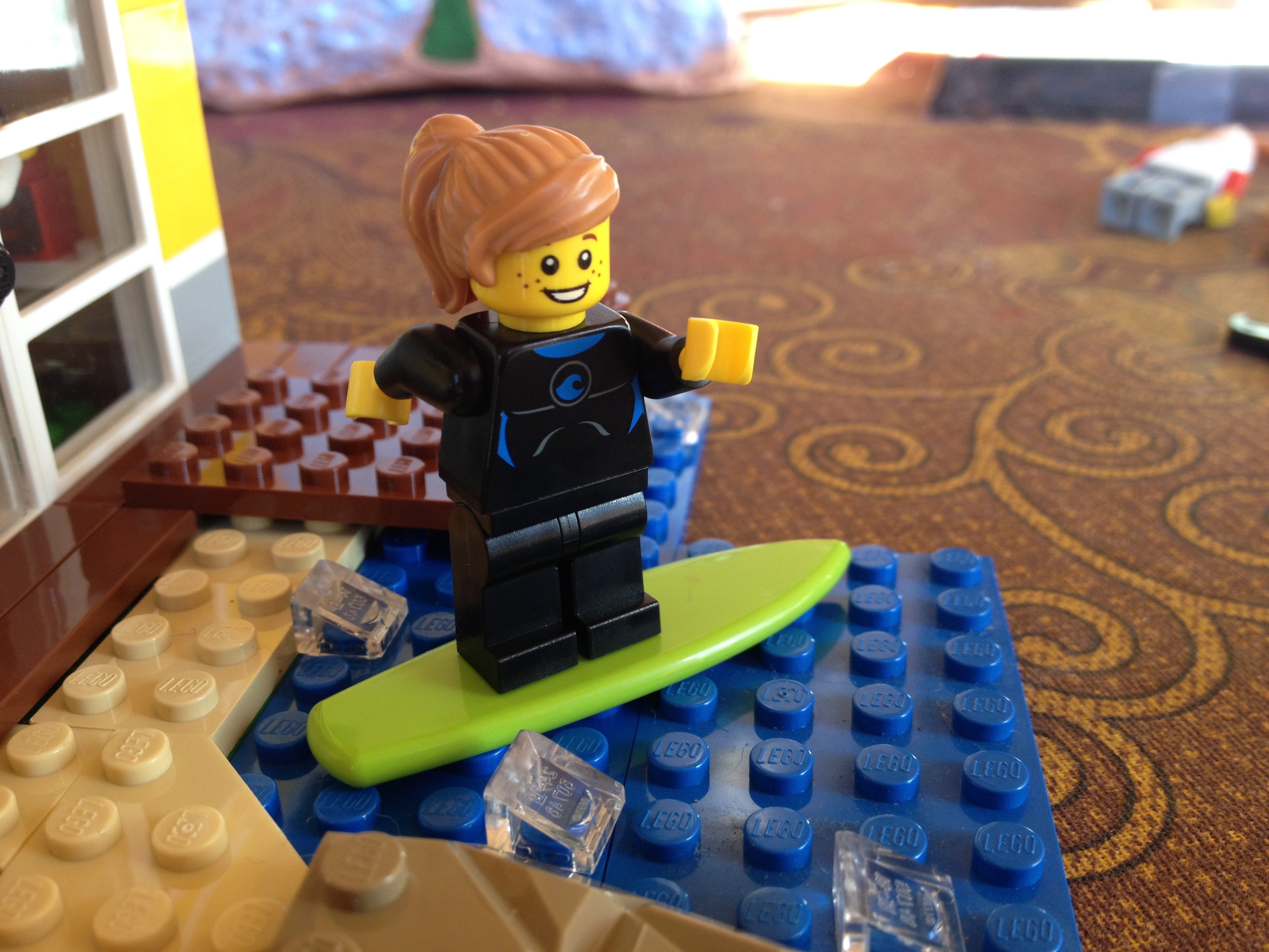 A lego girl with blond hair is surfing on a green lego surf board.