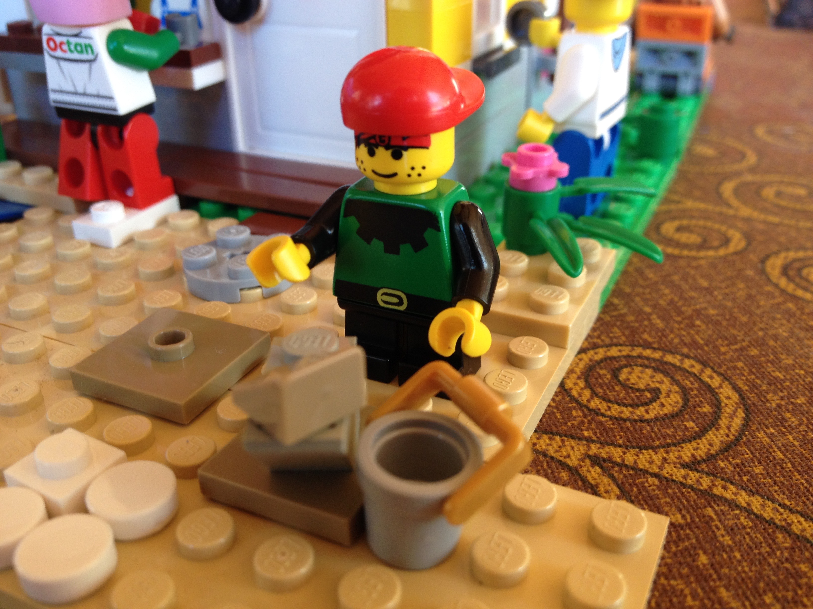 A cute little lego kid with a red baseball cap is building a lego sandcastle on the beach.