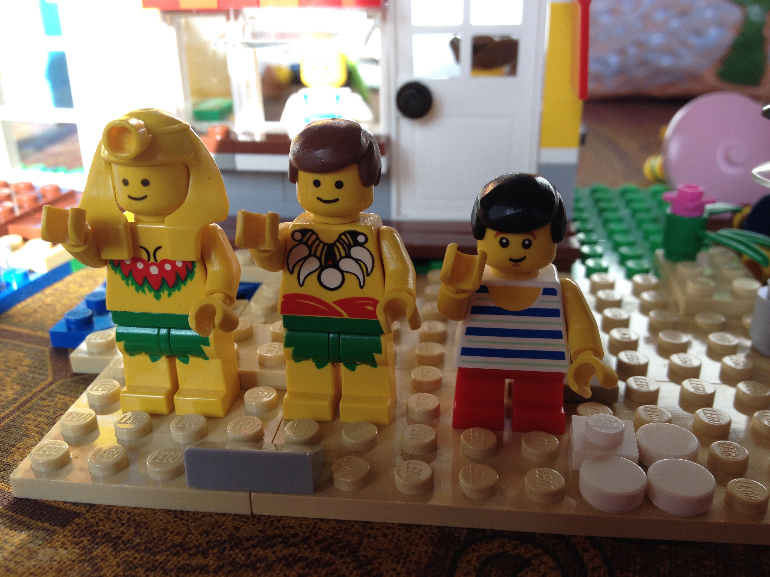 A lego boy is doing a dance with 2 lego people is hula costumes.